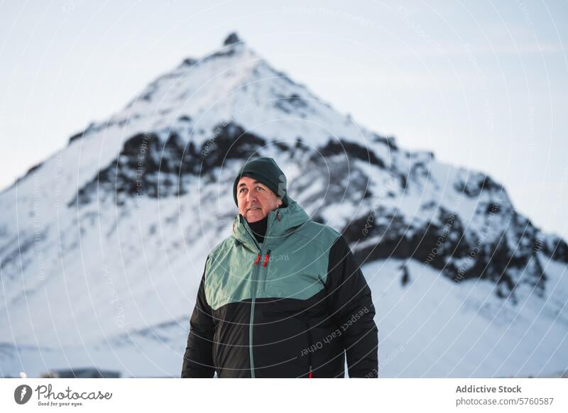 Ein warm gekleideter Mann steht im Vordergrund, den Blick auf den Gipfel eines majestätischen schneebedeckten Berges in Island gerichtet Schnee Berge u. Gebirge