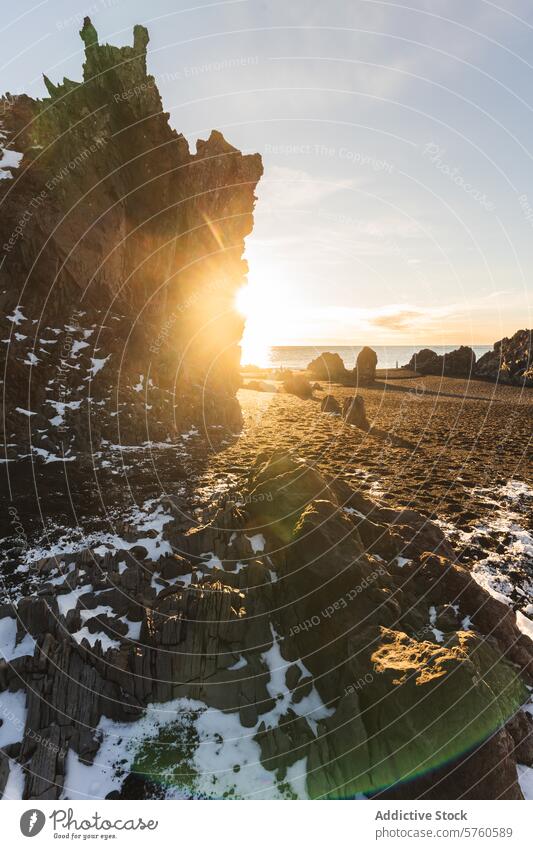 Die Sonne umspielt eine zerklüftete Basaltklippe an einem isländischen Strand und hebt die beeindruckenden geologischen Formationen und den zarten Hauch von Schnee hervor
