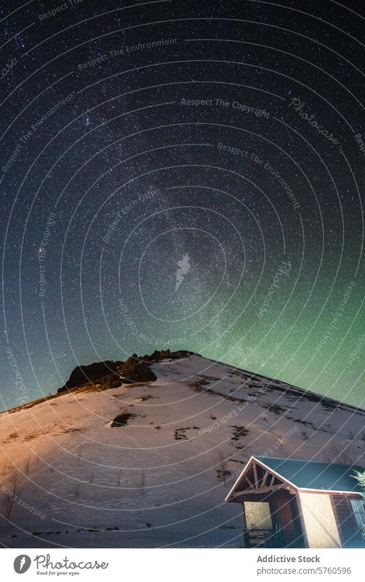 Ein atemberaubender Blick auf den Sternenhimmel und die subtilen Nordlichter über einem verschneiten Hügel, neben einer urigen isländischen Hütte sternenklar