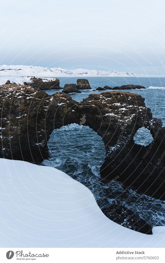 Der natürliche Bogen aus Vulkangestein steht inmitten von Schnee und stürmischem Wasser an der wunderschönen Küste Islands. Winter Torbogen isländisch