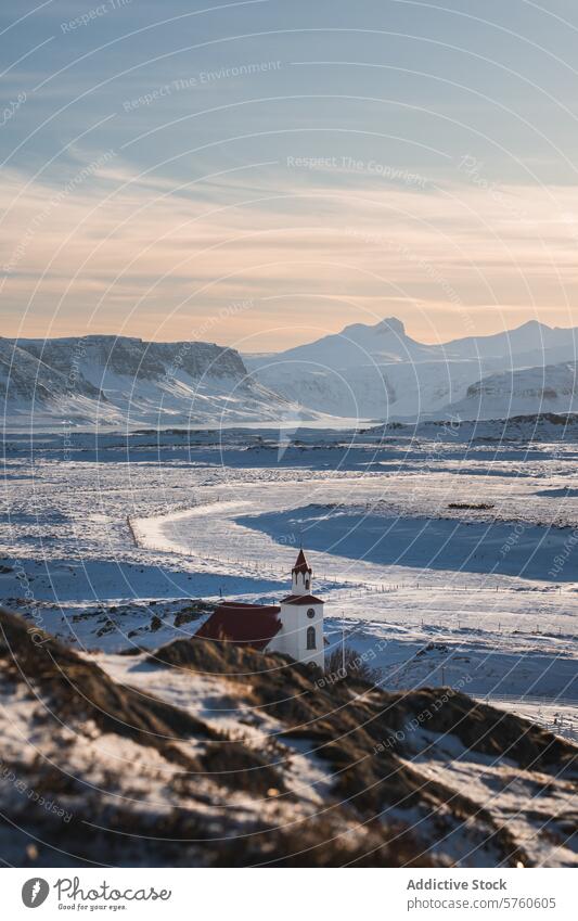 Eine malerische weiße Kirche mit rotem Dach sticht in der weiten, schneebedeckten Landschaft Islands hervor, mit majestätischen Bergen unter einem klaren Himmel
