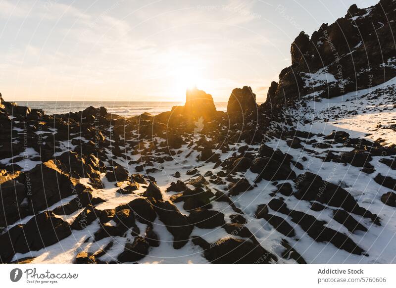 Die untergehende Sonne wirft ein warmes Licht auf die zerklüfteten, schneebedeckten Felsen einer isländischen Küste und schafft einen starken und schönen Kontrast
