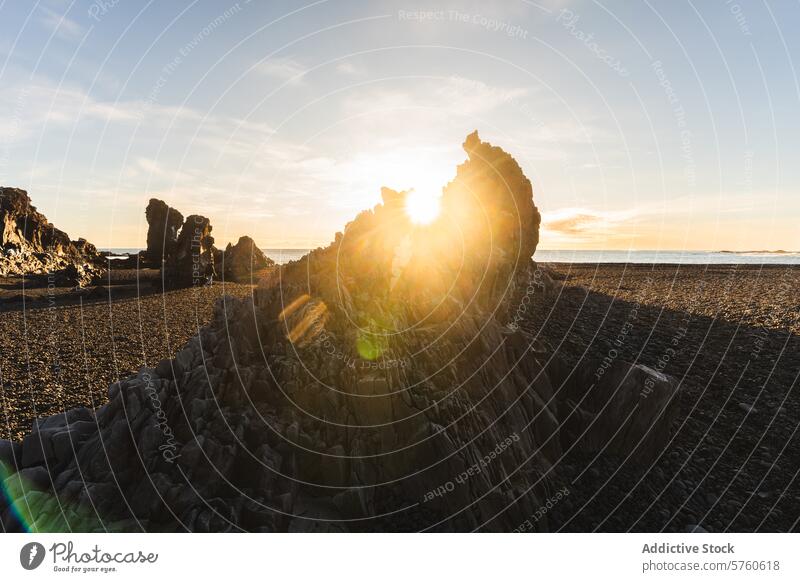 Ein fesselnder Sonnenstrahl bricht durch die einzigartigen Felsformationen an einem isländischen Kieselstrand und sorgt für einen dramatischen Start in den Tag