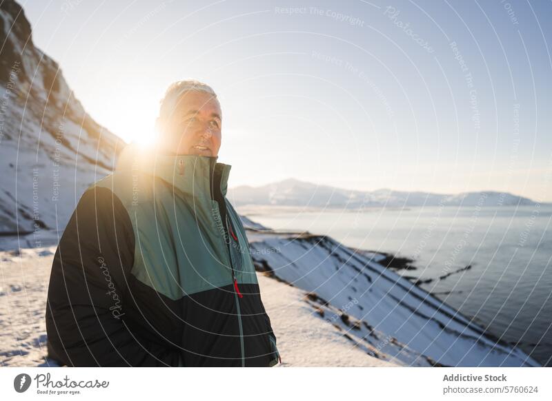 Ein Reisender in einem warmen Mantel genießt die ruhigen Momente eines sonnenbeschienenen Wintertages mit Blick auf die verschneite Küste von Island isländisch