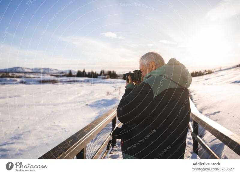 Ein Fotograf steht auf einer Brücke in Island, die Kamera in der Hand, und fängt die atemberaubende Winterlandschaft im sanften Licht der Sonne ein Fotokamera