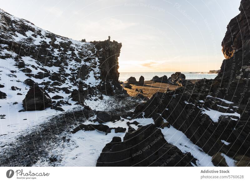 Das goldene Licht des Sonnenaufgangs taucht die einzigartigen Felsformationen und die schneebedeckten Klippen entlang eines isländischen Strandes in ein kontrastreiches Bild der Natur.
