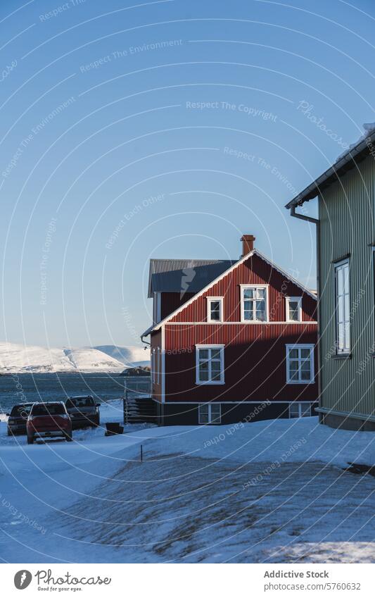 Ein traditionelles isländisches rotes Haus steht stolz vor einer gewaltigen Bergkette unter dem kristallklaren blauen Himmel eines kalten Wintertages heimwärts