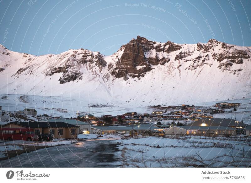 Ein gemütliches isländisches Dorf schmiegt sich an den Fuß hoher, schneebedeckter Berge, beleuchtet vom sanften Schein der Abenddämmerung Dämmerung Schnee