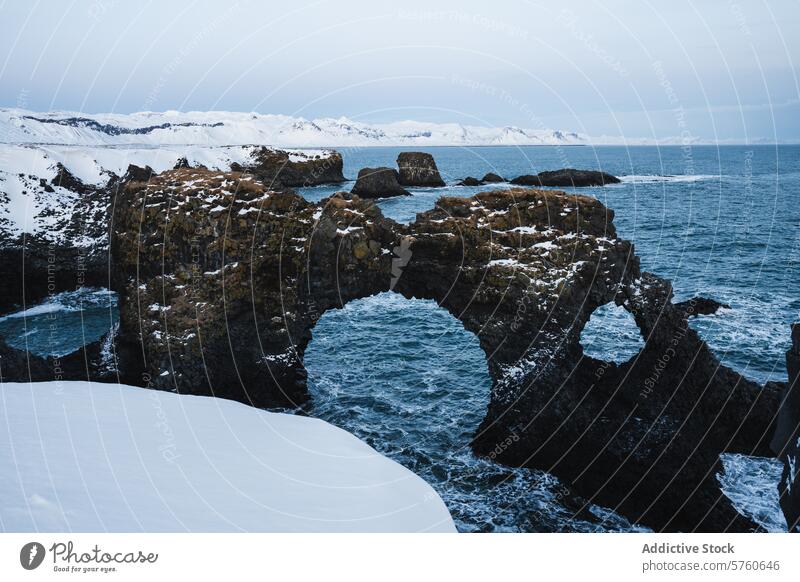 Der natürliche Bogen aus Vulkangestein steht inmitten von Schnee und stürmischem Wasser an der wunderschönen Küste Islands. Winter Torbogen isländisch