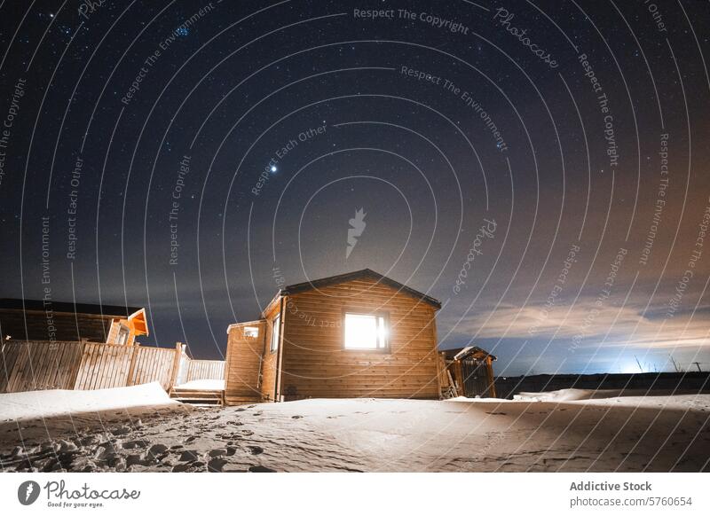 Eine gemütliche Holzhütte in Island, beleuchtet von einem sternenklaren Nachthimmel, bietet einen warmen Zufluchtsort inmitten der verschneiten Landschaft