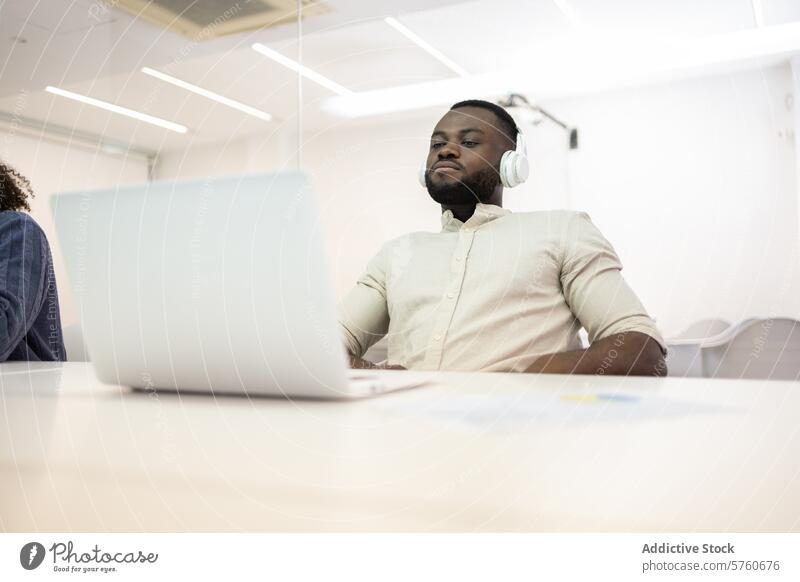 Afroamerikanische Fachkraft, die mit Kopfhörern arbeitet Afroamerikaner Mann professionell Büro arbeiten Laptop Wegsehen korporativ Business Schreibtisch
