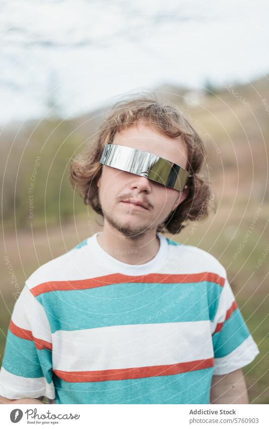Ein junger Mann posiert mit einer einzigartigen, verspiegelten Sonnenbrille, die in einer natürlichen Umgebung im Freien eine coole und moderne Ausstrahlung hat.