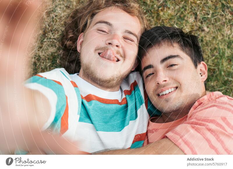 Ein zärtlicher Moment des Augenkontakts und des Lächelns zwischen einem schwulen Paar, beide Transgender, die sich auf dem Rasen umarmen Umarmen Gras Angebot