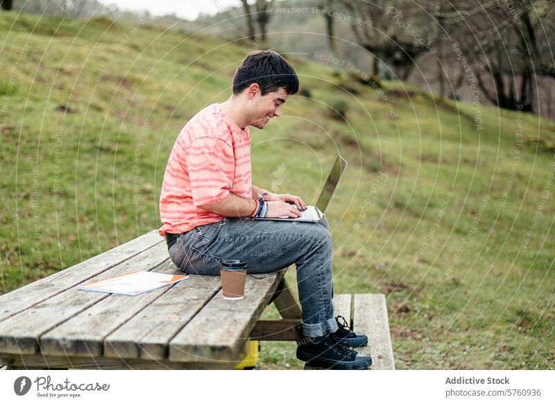 Ein Mann ist tief in seine Arbeit am Laptop vertieft, während er allein an einem hölzernen Picknicktisch sitzt, umgeben von der Stille der Natur im Freien Tisch