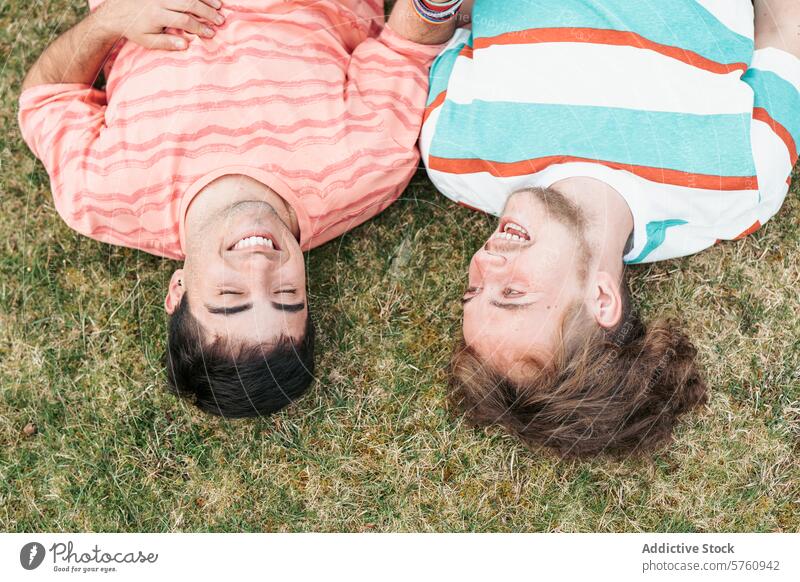 Draufsicht auf zwei Männer, ein verliebtes Paar und beide transsexuell, die einen Moment purer Freude und Lachens teilen, während sie im Gras liegen lachen