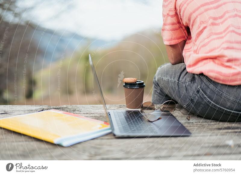 Ein ruhiger Arbeitsbereich auf einem rustikalen Holztisch im Freien mit Laptop, Kaffeetasse und Notizblock, umgeben von der Ruhe der Natur hölzern Tisch Tasse