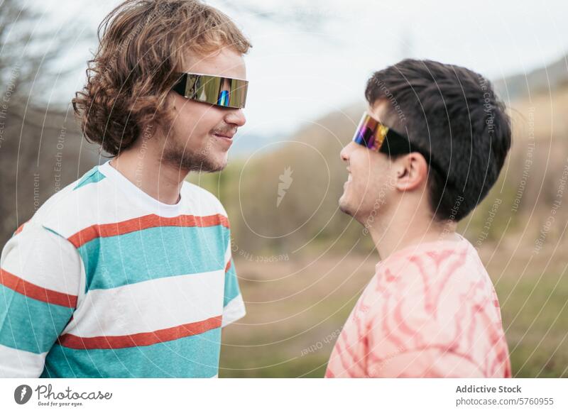 Ein enger Moment zwischen zwei Männern, die elegante, verspiegelte Sonnenbrillen tragen, was auf eine Verbundenheit oder ein gemeinsames Verständnis in einer Umgebung im Freien hindeutet