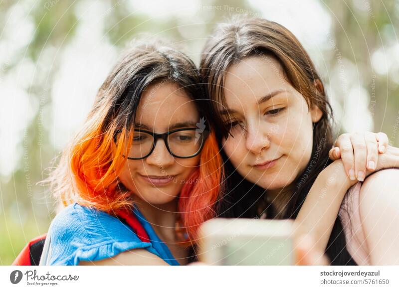Zwei junge Mädchen umarmen sich gegenseitig, während sie auf das Handy schauen, um ein Selfie zu machen Frau Person Frauen Freundschaft Porträt Lifestyle
