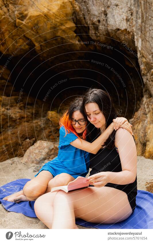 Ein verliebtes Pärchen kuschelt sich an einem Sommertag am Strand aneinander und liest ein Buch Person Freundschaft Lifestyle jung Freunde zwei Frauen