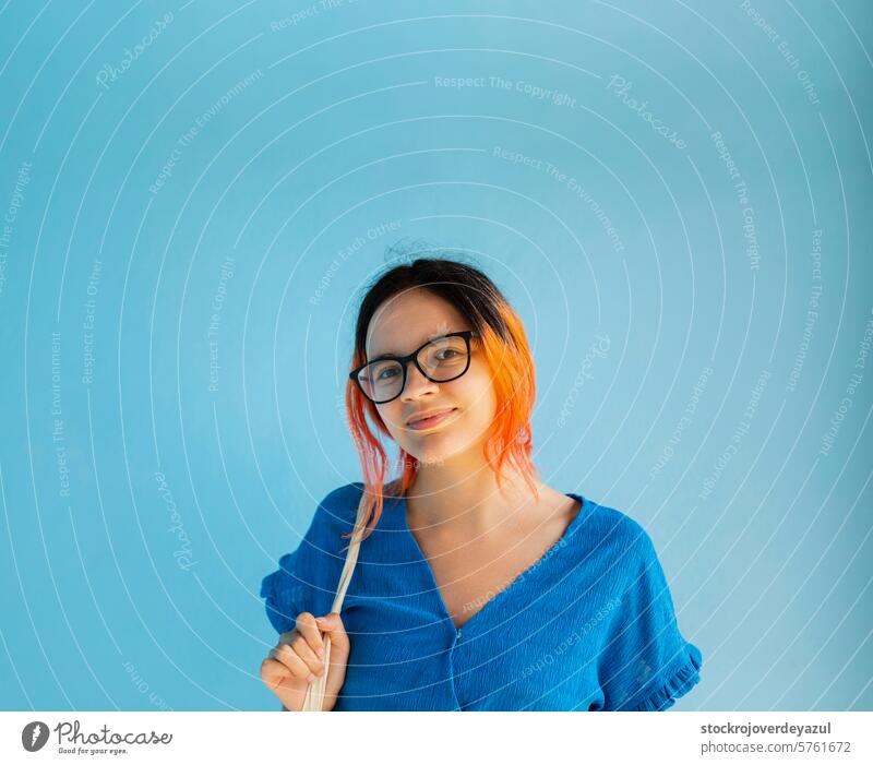 Ein junges Mädchen mit orangefarbenen Haaren blickt lächelnd in die Kamera, auf einfarbig blauem Hintergrund orangefarbenes Haar Frau Schönheit Person Glück