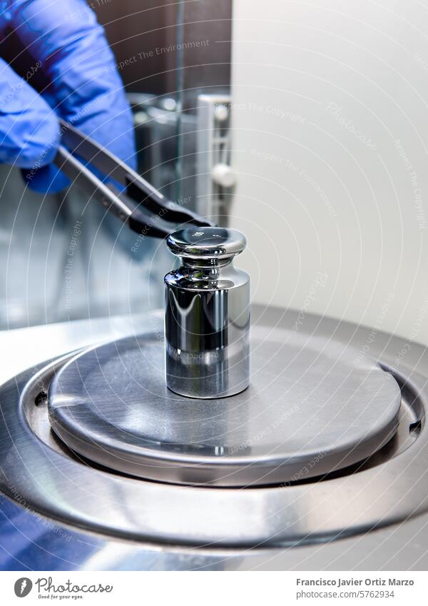 Die Hand des Bedieners hält ein Kalibrierungsgewicht aus Stahl, das auf die Analysenwaage gelegt wird. Konzept der Qualitätskontrolle in einem Labor.