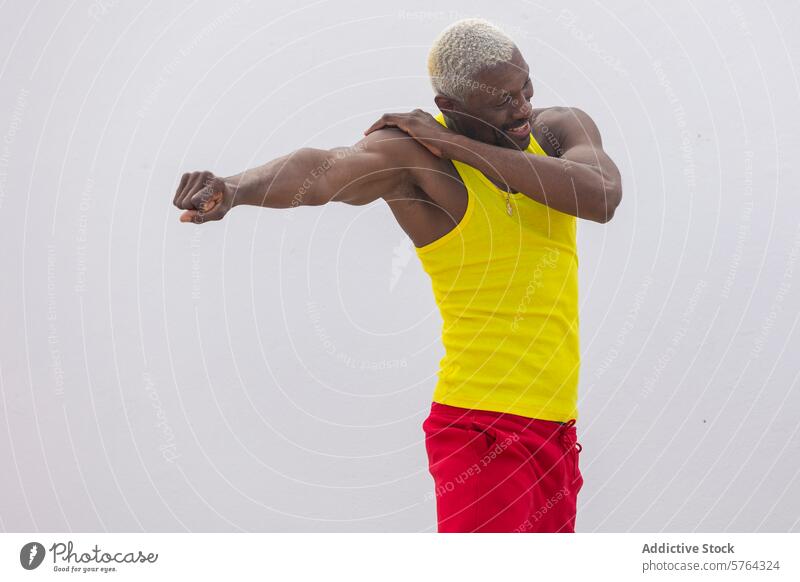 Ein fröhlicher Mann in einem leuchtend gelben Tank-Top und roten Shorts streckt seinen Arm aus und zeigt damit einen gesunden, aktiven Lebensstil Fitness