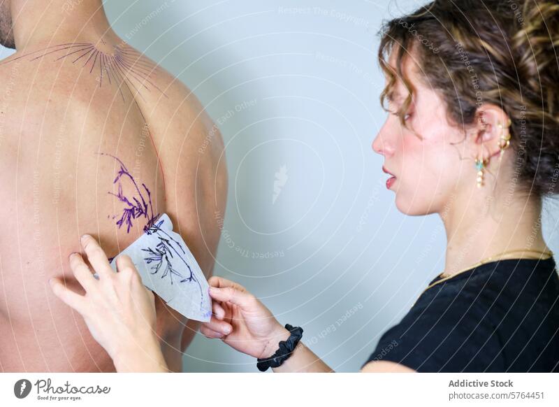 Tätowierer beim Anbringen des Designs auf dem Rücken eines Kunden Tattoo Künstler Frau Mann Schablone geblümt Vorbereitung Atelier transferieren Klient Haut