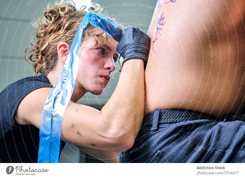 Tätowiererin bei der Arbeit in einem Studio Tattoo Künstler Frau Atelier Klient Tusche Design Haut Tätowierung professionell Konzentration Handschuh Hygiene