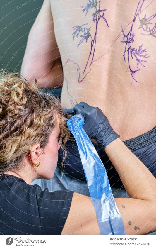 Tätowiererin bei der Arbeit am Rücken eines Kunden im Studio Frau Tattoo Künstler Atelier männlich Klient Tusche Design professionell erschaffend Tätowierung