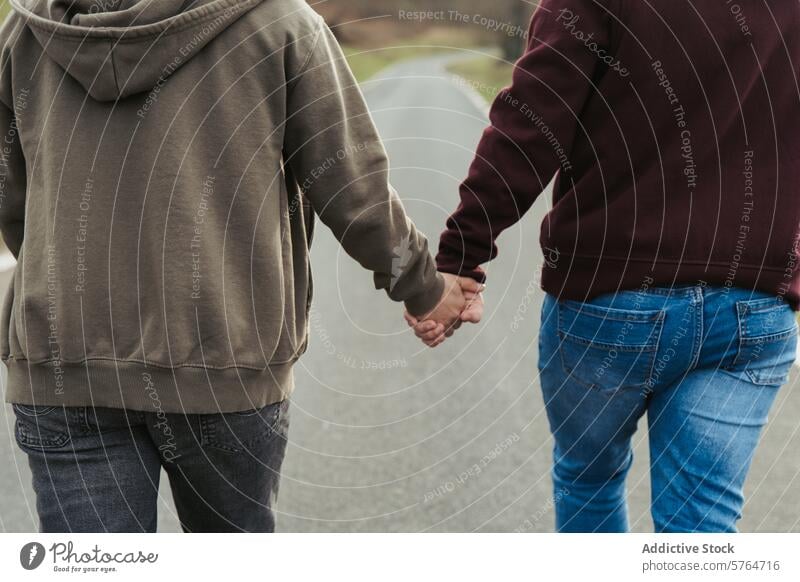 Nahaufnahme eines anonymen Paares, das sich an den Händen hält, wobei der Schwerpunkt auf den ineinander verschlungenen Fingern liegt, die Liebe und Verbindung bei einem ruhigen Spaziergang symbolisieren
