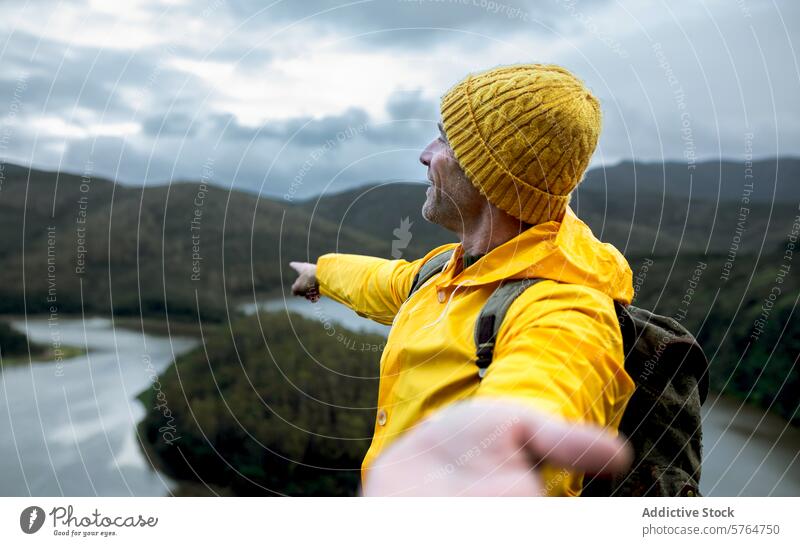 Abenteuerlustiger Mann mit Blick auf eine Flussschleife im Winter Irrfahrt übersehen malerisch Landschaft Natur im Freien reisen Erkundung Hut Regenmantel gelb