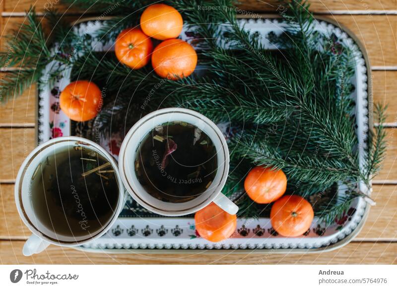 zwei Tassen mit Kräutertee auf einem Tisch mit Mandarinen und einem Fichtenzweig schwarz braun Chalet Weihnachten kalt Paar Becher für immer grau Hüte heiß Haus