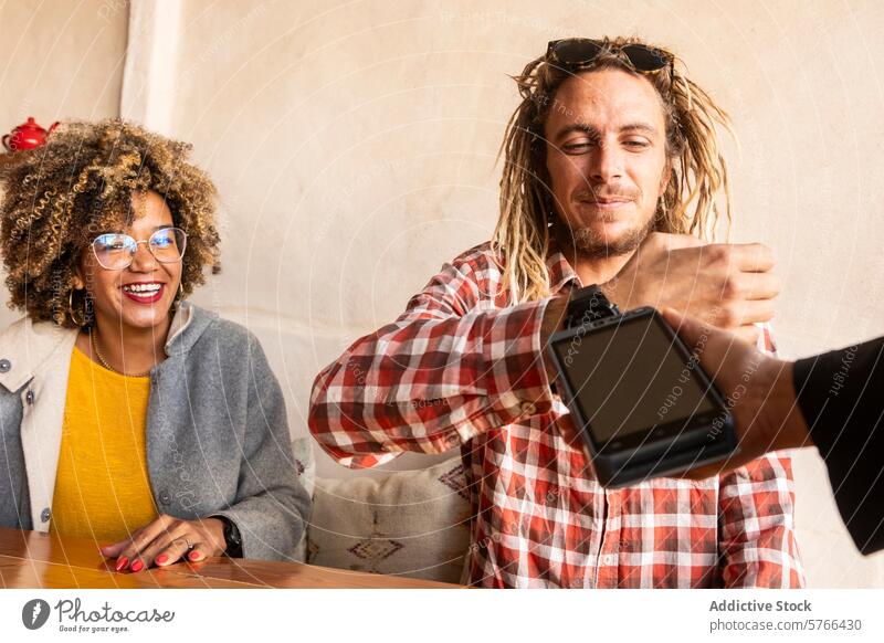 Fröhliche Freunde teilen sich die Bezahlung in einer gemütlichen Bar Rasta schwarze Frau Afro-Look multiethnisch Afrohaar Freude Zahlung smartwatch