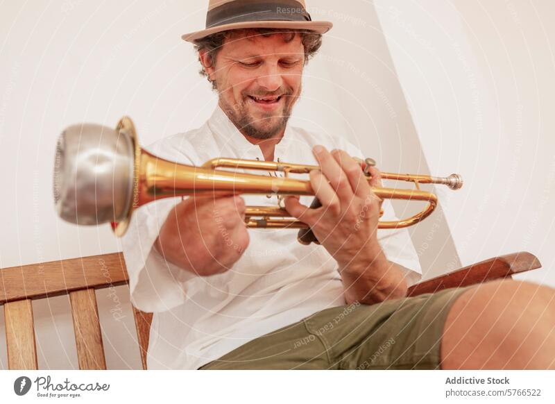 Lächelnder einarmiger Mann, der zu Hause Trompete spielt Musiker üben heimwärts im Innenbereich heiter Hut sitzend hölzern Stuhl Blechblasinstrumente Hobby