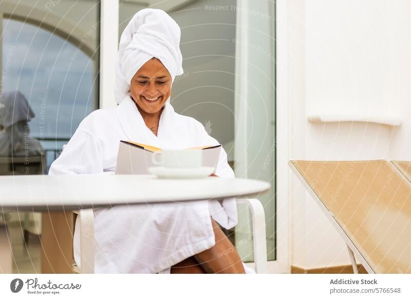 Hispanische Frau mittleren Alters im Bademantel genießt ein Buch und einen Kaffee auf einem Balkon Handtuch Lächeln lesen Erholung Morgen Freizeit Gelassenheit