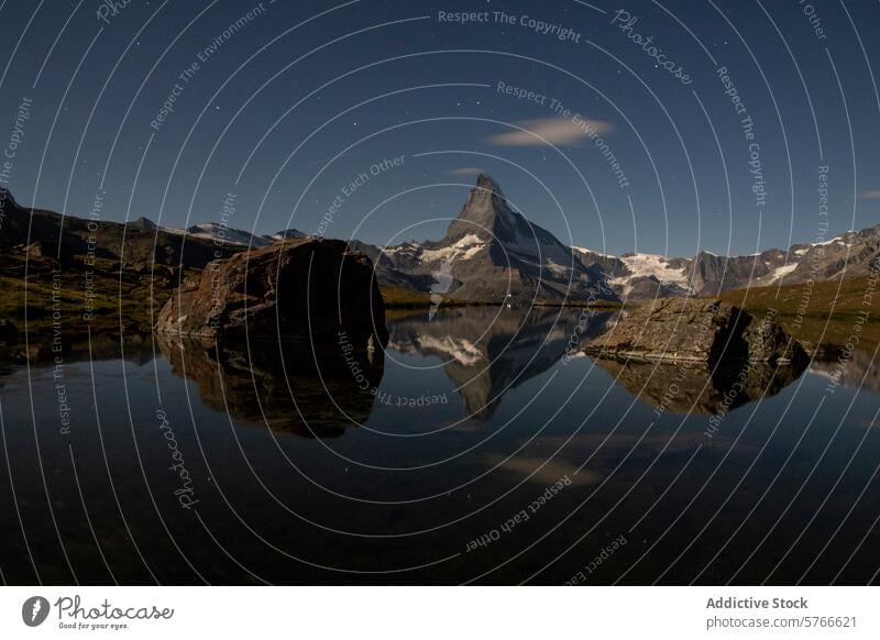 Unter dem Sternenhimmel spiegelt sich das Matterhorn perfekt im ruhigen Stellisee, und ein großer Felsblock verleiht der nächtlichen Alpenlandschaft zusätzliche Dramatik