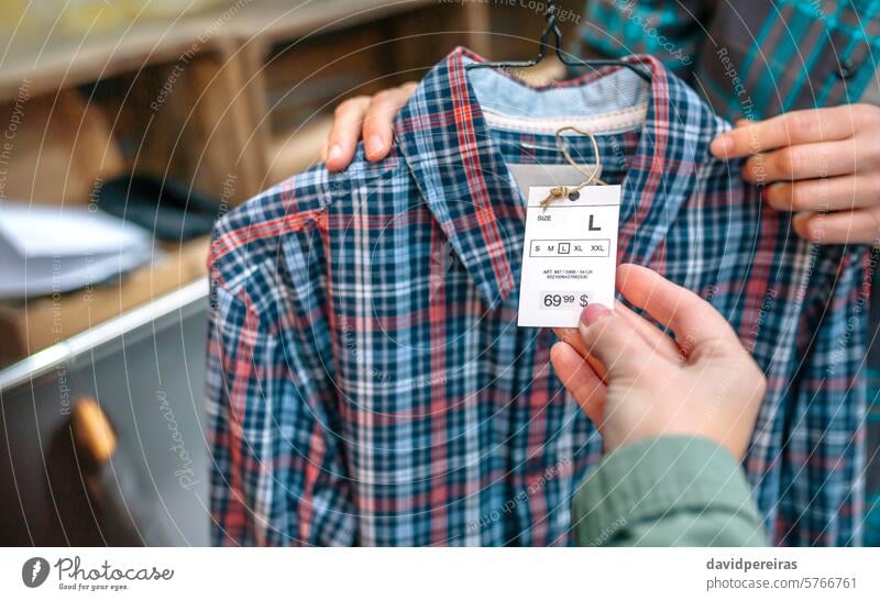 Nahaufnahme einer nicht erkennbaren Frau, die das Etikett eines karierten Hemdes in einem Bekleidungsgeschäft in der Hand hält unkenntlich Kunde Klient kaufen