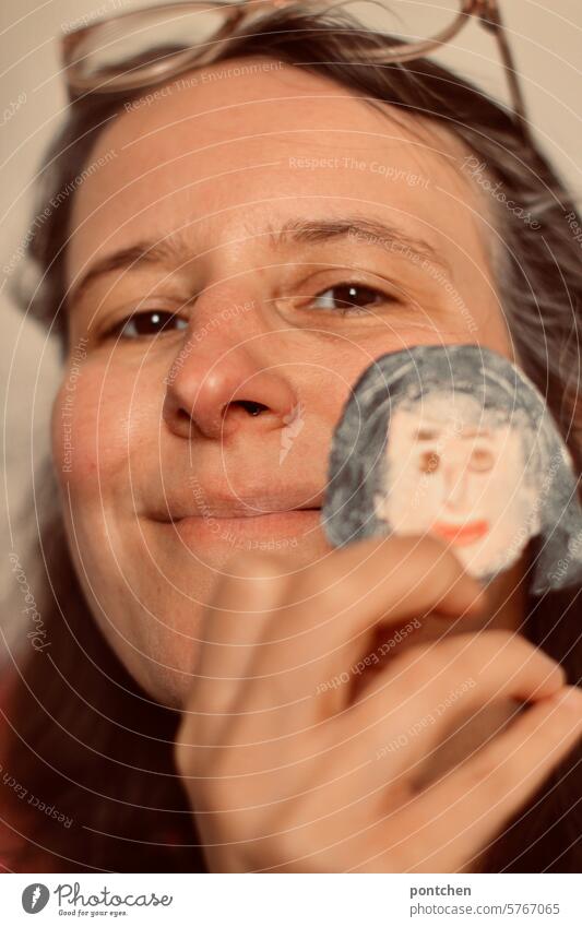 alter Ego. ein lächelnde Frau hält ein weibliches Gesicht aus Salzteig neben das eigene Gesicht frau salzteig gesicht vergleich alter ego kreativität basteln