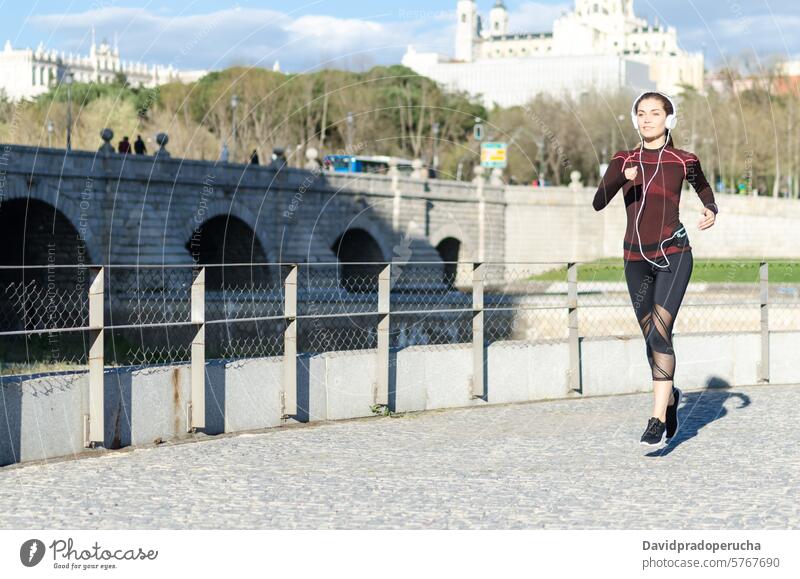 Frau, die sich nach dem Laufen und Joggen in einem Park mit Sportkleidung dehnt und ausruht laufen rennen Fitness strecken Übung jung Musik hören Kopfhörer