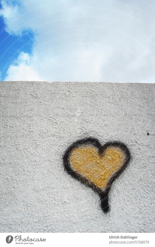 Herzgraffiti ,schwarzer Rand mit Gold gefüllt,auf weißer Mauer mit Himmel im oberen Drittel Liebe Freundschaft Freude Graffiti Spaß Optimismus Herzlichkeit
