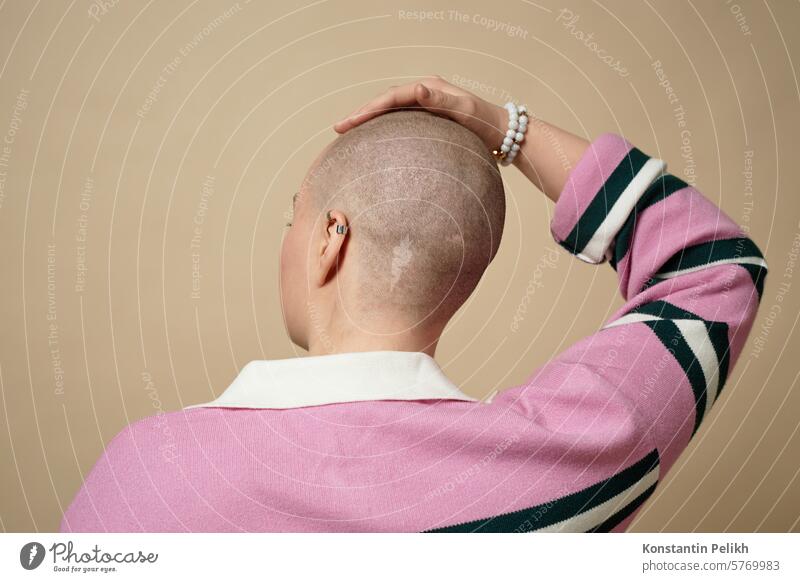 Rückenansicht einer jungen Frau mit Glatze, die ihren haarlosen Kopf im Studio berührt, Konzept für Alopezie und Krebsüberlebende kahl Mädchen gen z Haarausfall