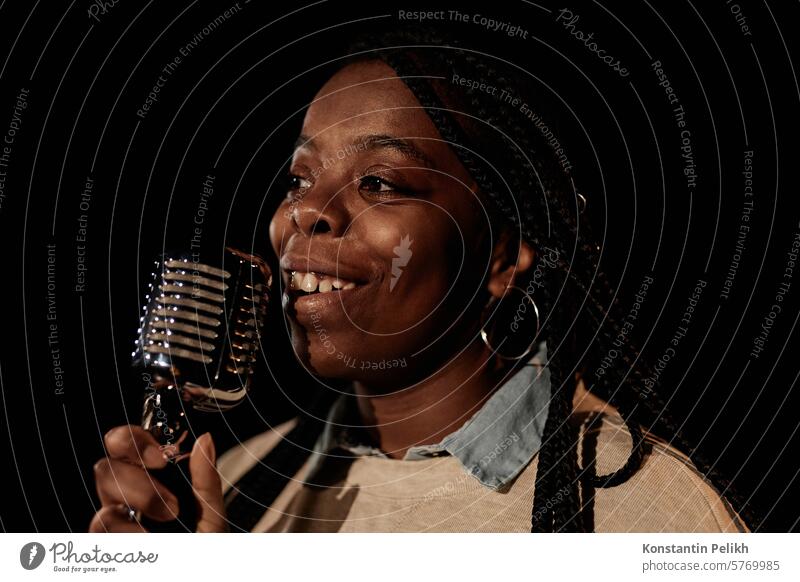 Closeup-Porträt von lächelnden afroamerikanischen Frau hält Mikrofon während der Durchführung auf der Bühne mit schwarzem Hintergrund Kopie Raum singen Gesang