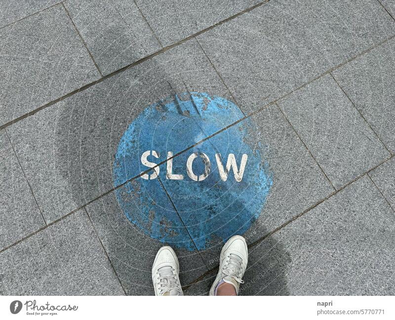 Top shot Bürgersteig mit Füßen vor aufgemaltem SLOW Icon. slow Entschleunigung langsam Tempo Geschwindigkeit stressabbau stressbewältigung