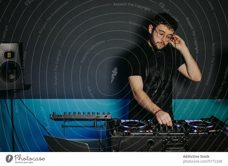 Konzentrierter DJ beim Einstellen der Tontechnik in einem Club dj männlich jung Klang Gerät Mixer dunkel Kopfhörer Einstellung konzentrierend Musik