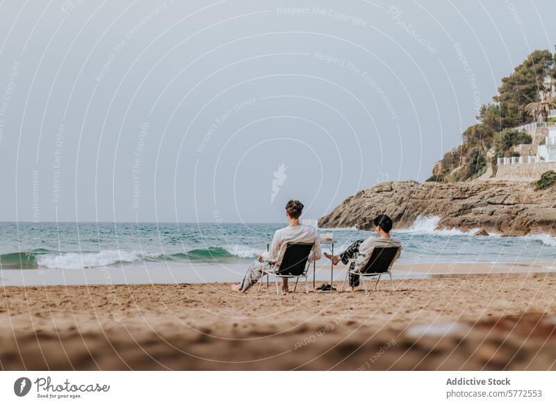 Ruhige Strandszene mit zwei Menschen, die sich am Meer entspannen MEER sich[Akk] entspannen Stuhl winken Ufer Sand einzeln felsig Hügel Hintergrund ruhig