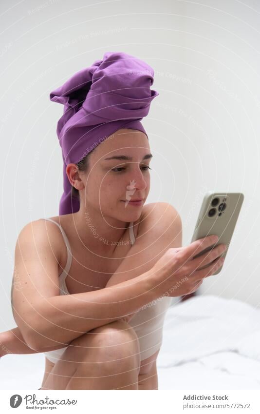Frau mit Handtuch auf dem Kopf, die nach dem Duschen im Telefon surft Smartphone Bett Routine Browsen Sitzen Schlafzimmer Telefonbildschirm Handtuchwickel