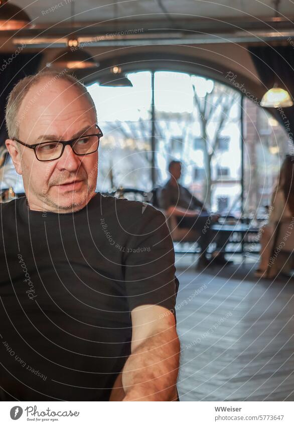 Ein Mann sitzt in einem Cafehaus mit interessanter Architektur und schaut skeptisch Herr Person Restaurant Lokal Gaststätte Bogen industriell historisch Mimik
