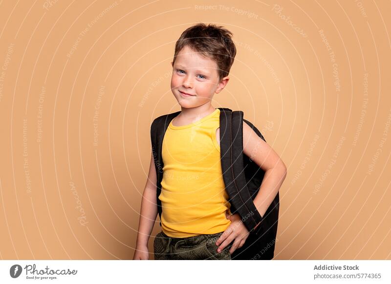 Selbstbewusster Junge bereit für die Schule auf beigem Hintergrund Kind Rucksack selbstbewusst Lächeln frech jung Schüler gelb ärmelloses Hemd