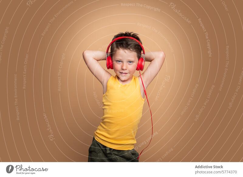 Junger Junge genießt Musik mit roten Kopfhörern Kind Lächeln gelb Entertainment hören posierend selbstbewusst Hintergrund braun Tanktop pulsierend Glück Genuss