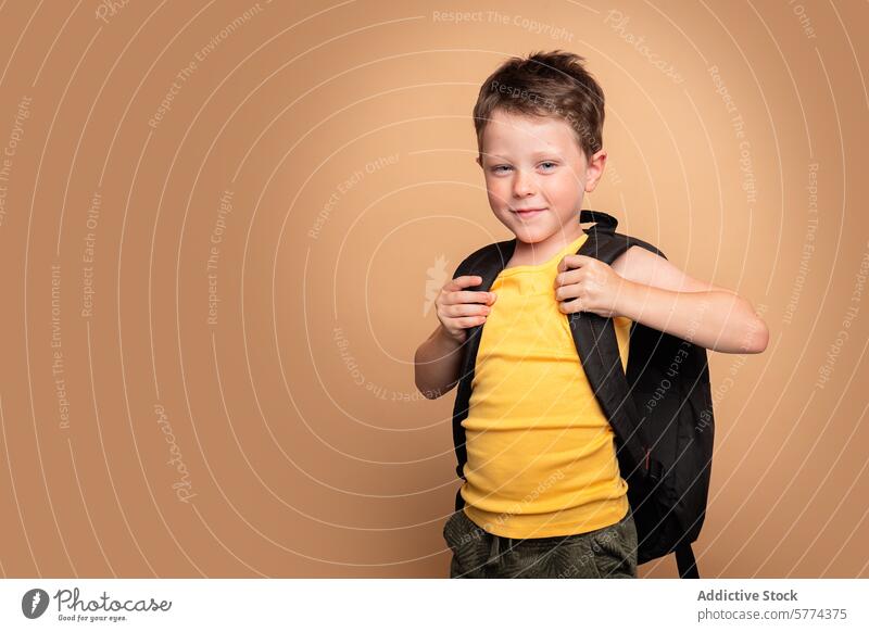 Junge mit einem Rucksack bereit für die Schule Kind Schüler Bildung selbstbewusst Lächeln jung beiger Hintergrund Schuljunge Kindheit lässig Pose heiter Glück